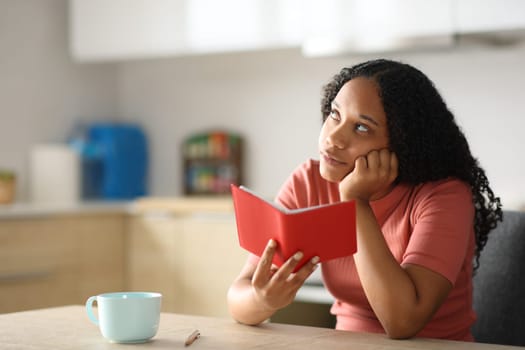 Black woman holding paper agenda thinking in a kitchen at home