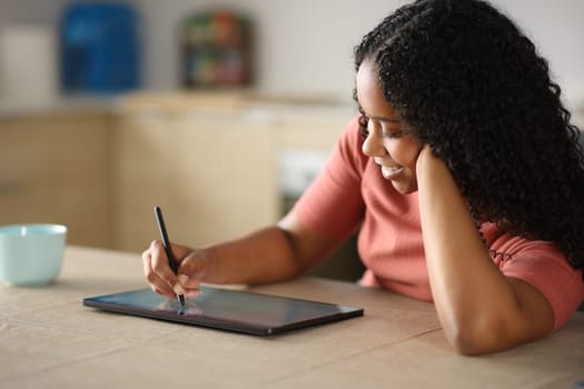 Black woman in a kitchen using tablet and pen at home