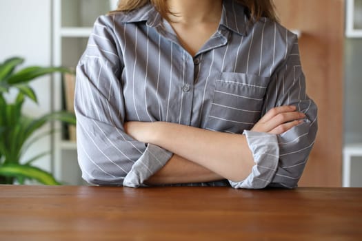 Front view close up portrait of a woman folding arms in a wooden table at home