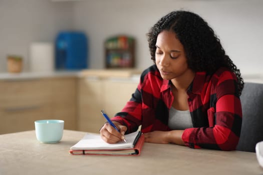 Concentrated black student learning writing notes in the kitchen at home