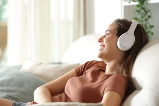 Happy woman listening audio on headphone sitting in a couch at home