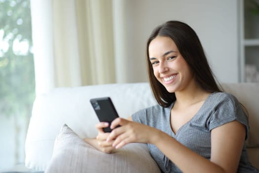 Happy woman posing holding mobile phone sitting in a couch at home