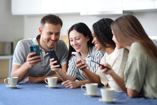 Happy interracial friends checking their mobile phones in the kitchen at home