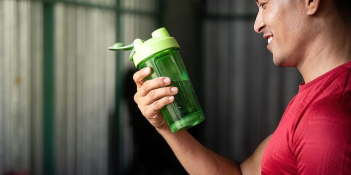A fit man smiles while holding a green shaker bottle filled with water, emphasizing the importance of hydration in fitness.