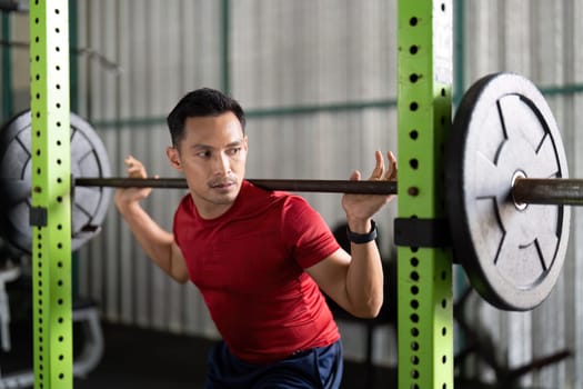 A dedicated male athlete focuses on his form while squatting with a barbell in a gym, emphasizing strength training.