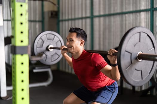 A focused male athlete performs squats with heavy weights, showcasing dedication to strength training in a gym.