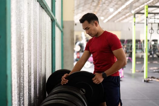 A focused male athlete adjusts weights at a gym, embodying dedication to fitness and strength training.