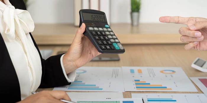 An accountant using a calculator to review financial reports during a business meeting, showcasing analytical skills and teamwork.