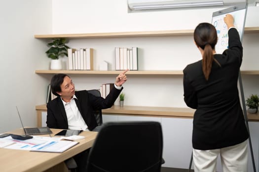 A male consultant points at a chart while discussing financial metrics with a female colleague in a meeting room.