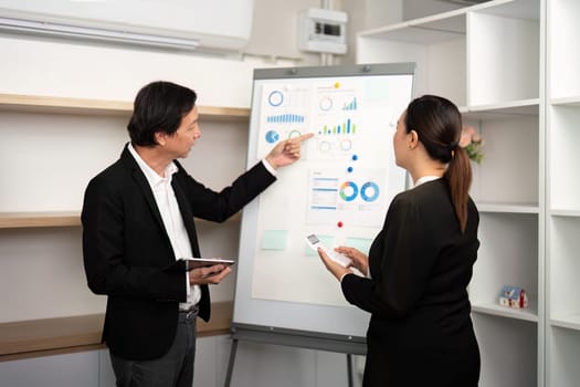 A male consultant discusses financial charts while a female colleague takes notes in a modern office.