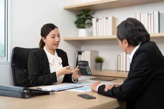 A financial consultant explains calculations using a calculator to a male client in a modern office setting.