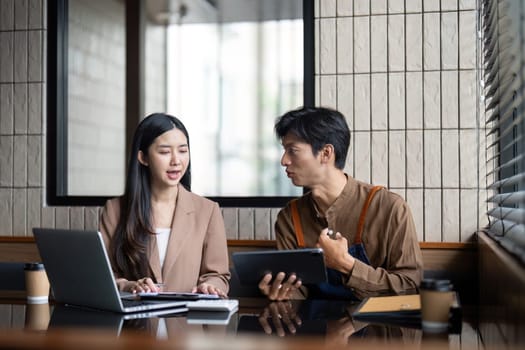 A man and woman engaged in a focused conversation, reviewing documents and digital content in a contemporary workspace.