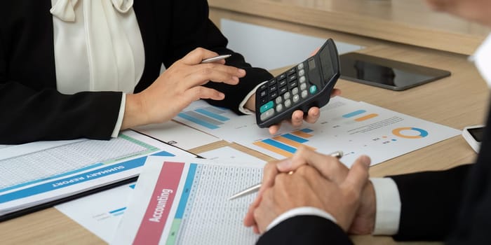 Two professionals discussing financial data and using a calculator while analyzing reports and charts on the table.