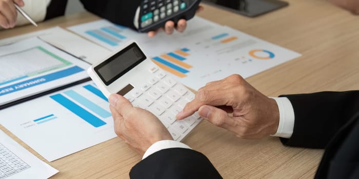 Close-up of a business professional using a calculator while analyzing financial reports and data during a meeting.