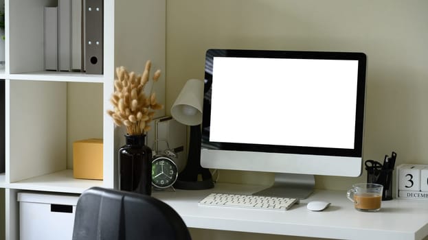Stylish home office scene with blank monitor screen, dried flowers in a vase, and coffee cup.
