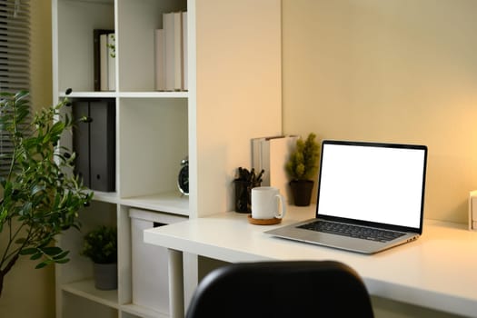 Minimalist home office setup with blank laptop screen, coffee mug, and organized shelf.
