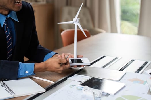 A businessman presents a wind turbine model, emphasizing sustainable energy solutions in an ESG meeting.