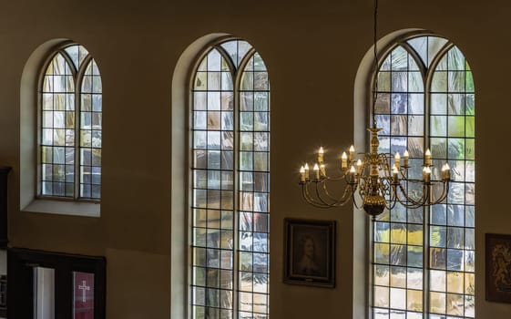 Royal Tunbridge Wells, UK - Apr 29, 2025 - A stunning view of Chandelier hanging from the ceiling and Large stained glass windows in the background inside of The Church of King Charles the Martyr. use it as your Wallpaper, Poster and Space for text, Selective focus.