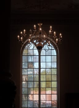 Royal Tunbridge Wells, UK - Apr 29, 2025 - A stunning view of Chandelier hanging from the ceiling and Large arched stained glass windows in the background inside of The Church of King Charles the Martyr. use it as your Wallpaper, Poster and Space for text, Selective focus.
