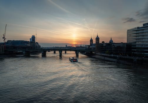 London, UK - Apr 27, 2025 - A stunning silhouette view of Cannon street railway station bridge with Cruise boat on River thames and colour sky in the background. use it as your Wallpaper, Poster and Copy space, Selective focus.