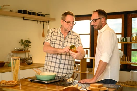 Happy senior man and grown son preparing pasta dish in a bright kitchen. Father day concept.