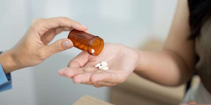 A healthcare worker dispenses pills from a prescription bottle to a patient hand, illustrating personal care and attention.