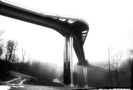 Black and white photo of a steel bridge over a river in fog. High quality photo