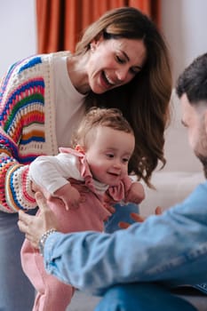 Mother and father encourage their baby girl as she takes her first steps on the carpet. A heartwarming family moment filled with love, support, and early childhood development at home. Vertical