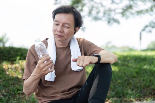 A happy senior man sitting outdoors, enjoying a refreshing drink of water after practicing yoga, emphasizing wellness and staying active.