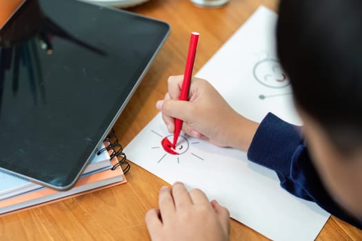 A young child uses a red pen to draw a smiling sun on paper, showcasing creativity and artistic development in a home setting.