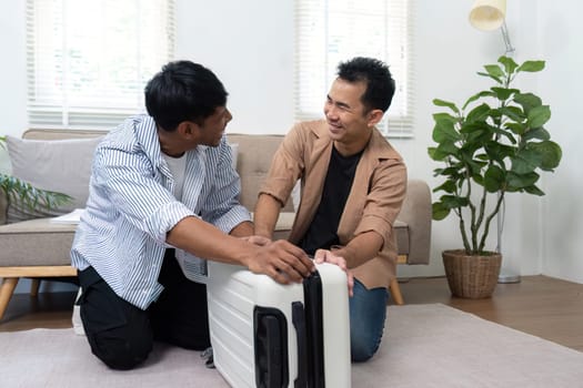Two men work together to pack their suitcase, sharing smiles and excitement as they prepare for their travel adventure.