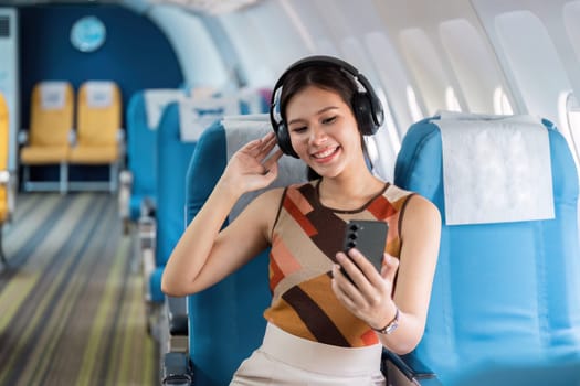 A joyful tourist enjoys inflight entertainment with her headphones on, showcasing a modern travel experience aboard an airplane.