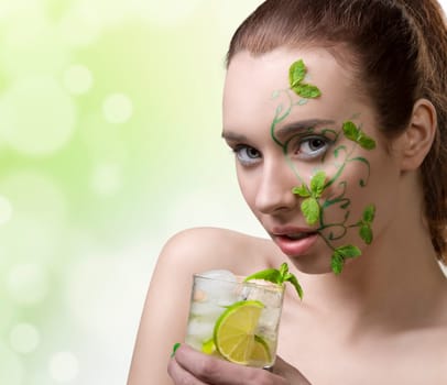 close-up portrait of pretty girl with green creative make-up and some mint leaves on the face, drinking mojito