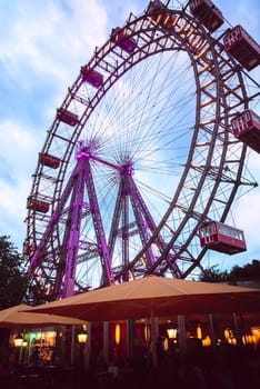 Historic Ferris wheel called Wiener Riesenrad in central public park or Prater park, Vienna, Austria, at cloudy dusk. Outdoor cafes