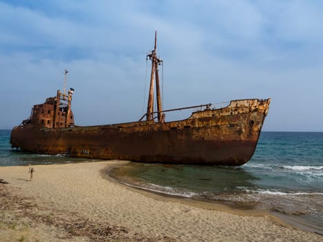 Rusty corroding Dimitrios shipwreck on a sandy beach near Gythio, Greece. A partially sunk rusty metal shipwreck decaying through time on a sandy easily accessible beach on a sunny day.