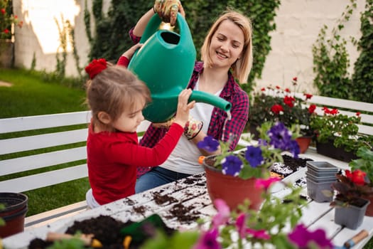 A child joyfully waters flowers alongside a smiling adult.