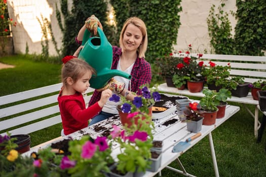 A young girl and her mother plant flowers joyfully outdoors.