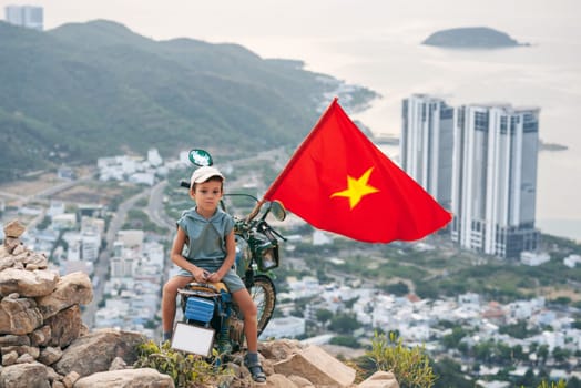 Tourist child boy on a motorcycle on top of a mountain with a Vietnam flag. Mountain of Angels in Nha Trang in Vietnam