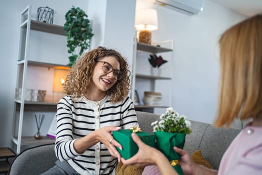 A woman is seen handing a wrapped present to friend, both smiling in a gesture of gift-giving and appreciation. Their body language indicates a moment of connection and joy.