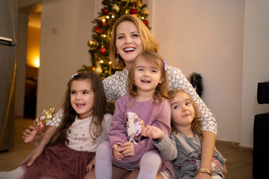 A mother happily embraces her three daughters in a cozy, decorated home.