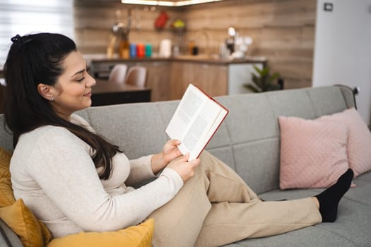Woman reading a book while relaxing on a sofa at home.