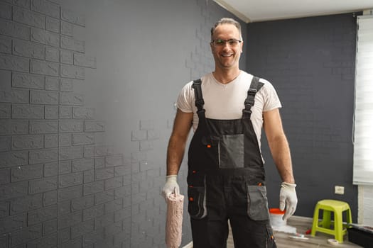Man stands in the room smiling, wearing protective gloves and holding a roller in his hand.