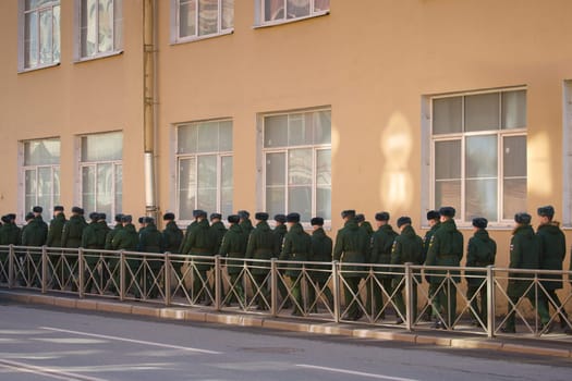 a column of cadets of military forces walk along the fence and gates with the symbols of the armed forces. High quality photo