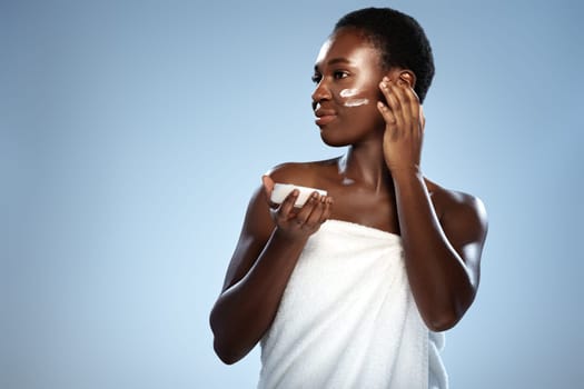 A woman stands in a bright studio, wrapped in a towel, gently applying cream to her face. The serene atmosphere enhances her skincare routine, promoting self-care and wellness.