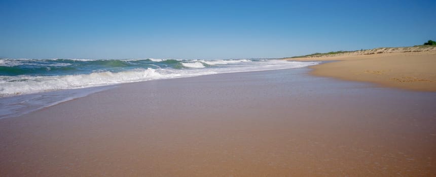 A beautiful day at Kawana Warana Beach, Sunshine Coast, Queensland. It's Autumn and the sky is blue, and the surf waves with big white foam tops break out wide, and roll towards the shore before crashing and flowing  across the sandy beach.