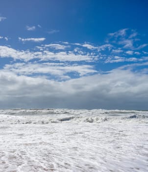 A coastal background image of very rough wild dangerous sea along the shoreline with blue sky and storm clouds on the horizon