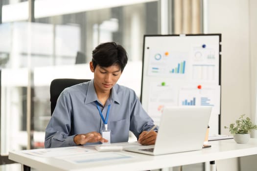 A young professional multitasks with a smartphone and laptop, demonstrating effective time management in a busy office environment.
