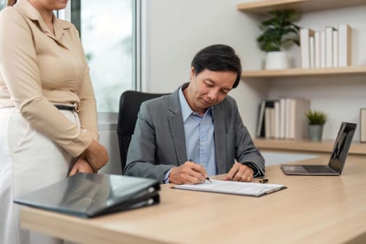 A businessman signs important documents while collaborating with a colleague, highlighting teamwork and professional integrity.