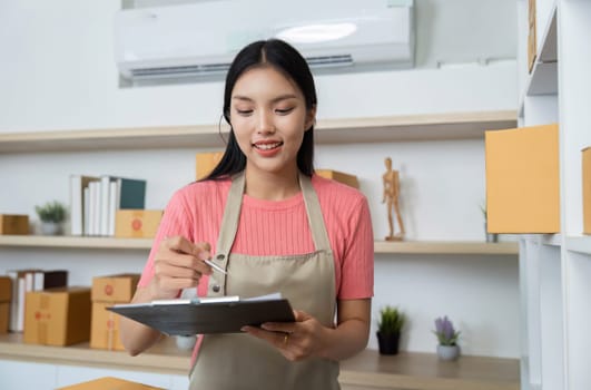 A female small business owner checks inventory and takes notes while smiling in her retail shop, showcasing her dedication and professionalism.