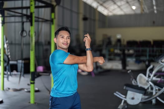 A fit man stretches his arms in a gym, focusing on flexibility and preparing for an intense workout session.